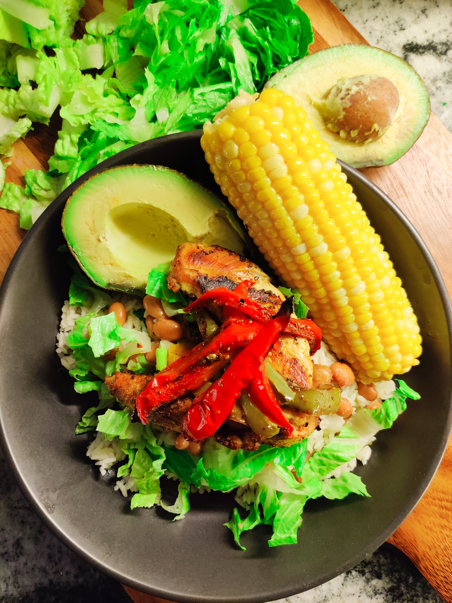 A bowl of fajita chicken on a bed of cilantro lime rice, with pinto beans, avocado, and lettuce. 